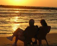 couple sitting on chairs on a beach at sunset